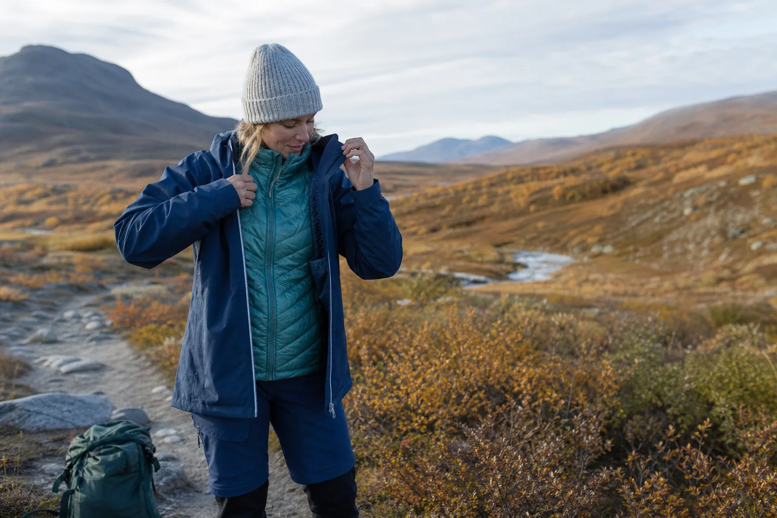 Vandrare i flerskiktskläder justerar mellanlagret på en stig i höstlandskap