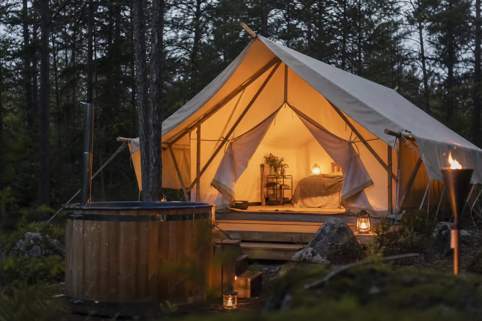 Inrett canvastält med säng och varmt ljus i skogsmiljö i skymning