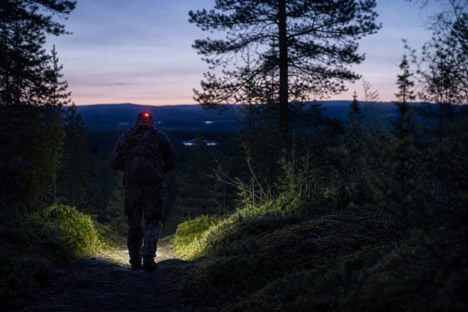 Jägare med kamouflagefärgad pannlampa i skogsterräng i gryning