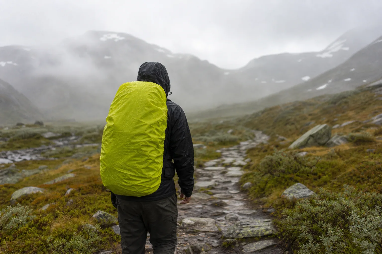 Vandringsryggsäck med regnskydd draget över i regnigt väder på en fjällstig
